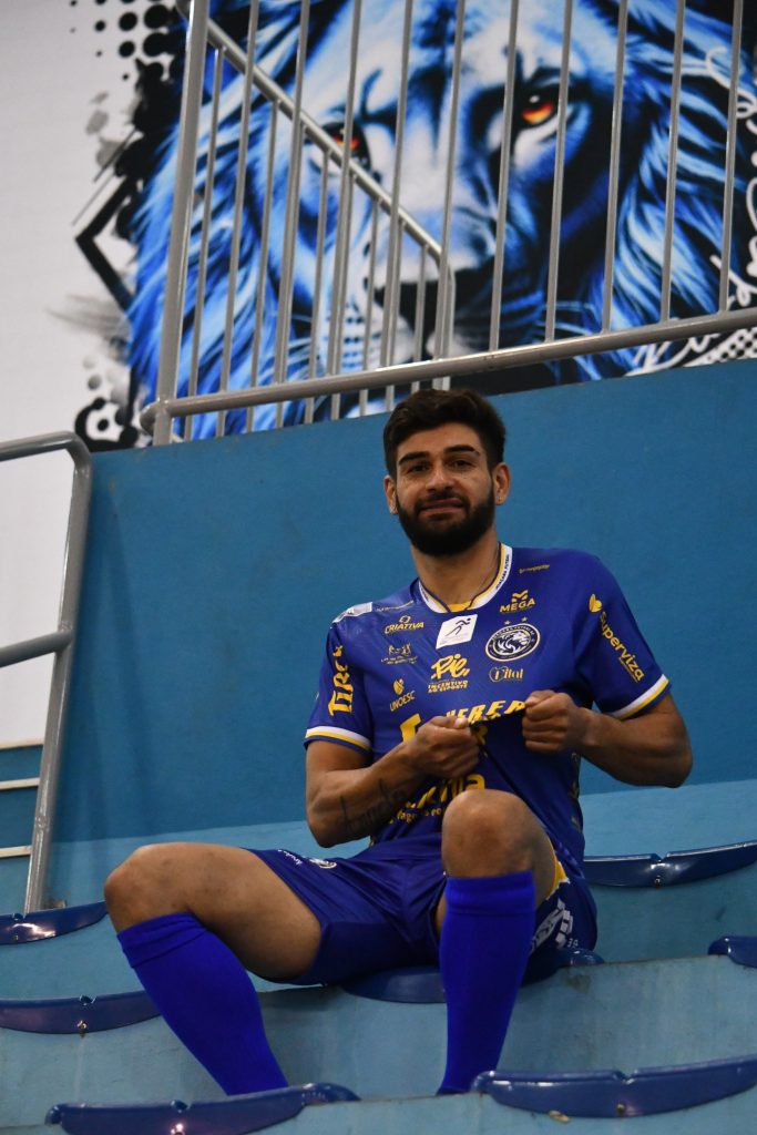 Dimas sentado na arquibancada, de camisa azul do Joaçaba Futsal