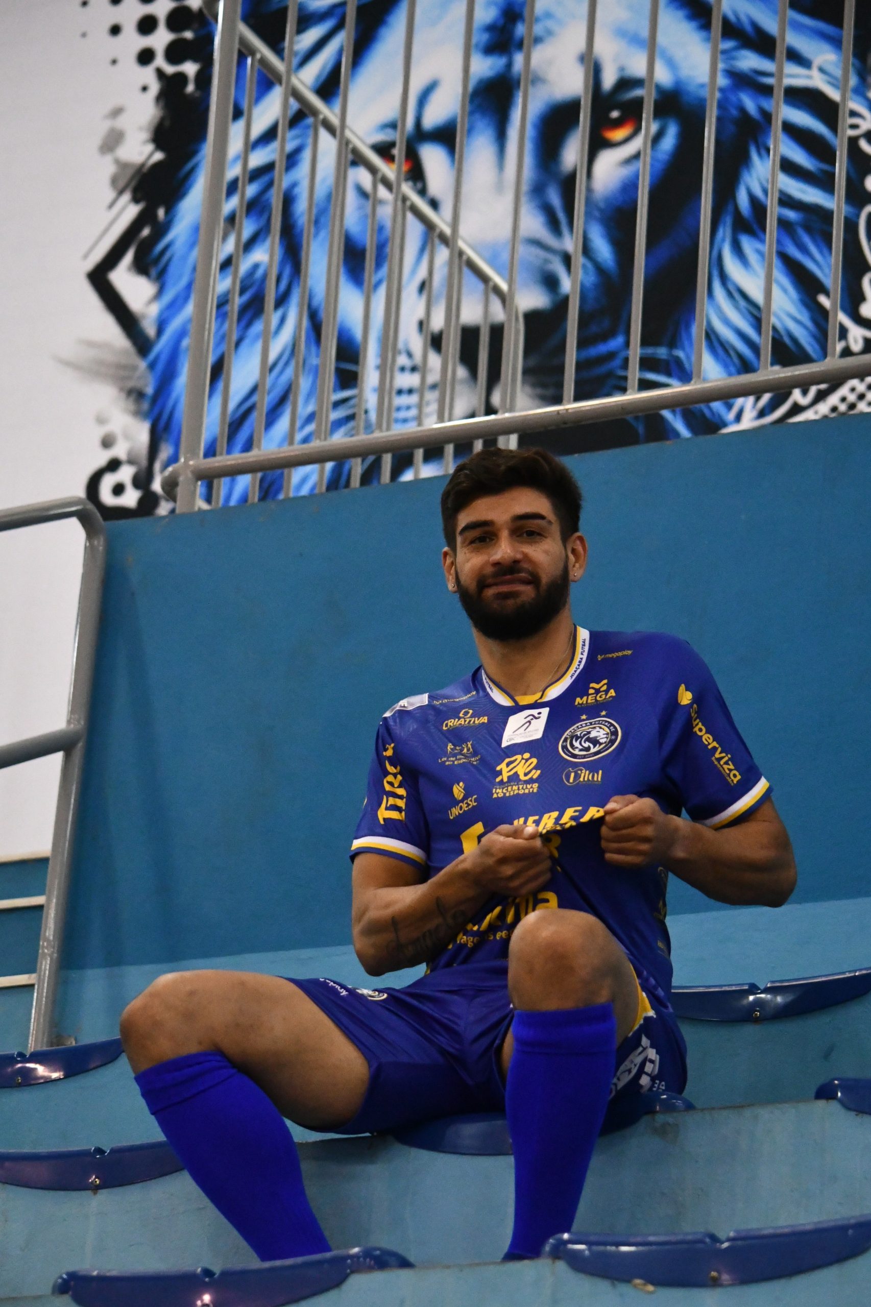 Dimas sentado na arquibancada, de camisa azul do Joaçaba Futsal