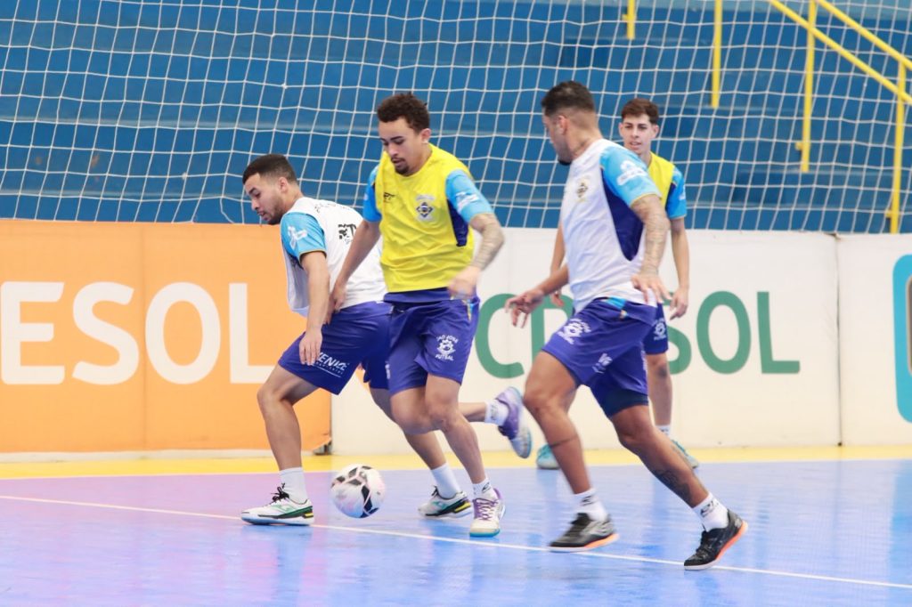 Atletas do São José Futsal disputam a bola em treino, em quadra com a marca da LNF Cresol ao fundo