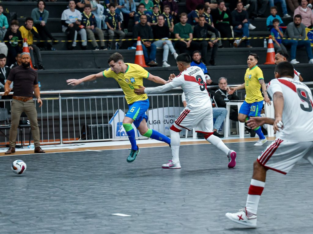 Atleta do Brasil, de camisa amarela, divide a bola com jogadores do Peru, de camisa branca e vermelha, na Arena Ivo Sguissardi, em Xanxerê